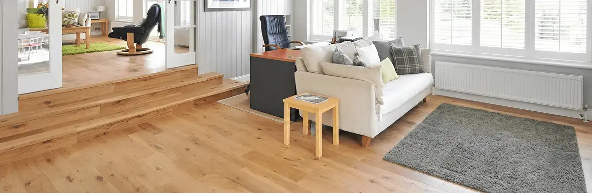 A modern living room with professionally installed laminate flooring, a beige sofa, a small side table, a gray rug, and large windows with white shutters in New Orleans, LA